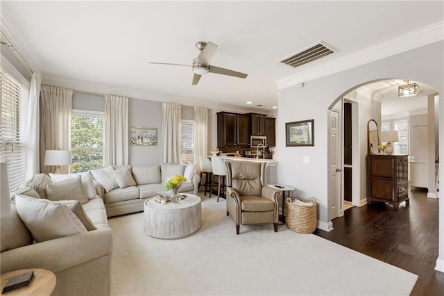 living room with a ceiling fan, visible vents, arched walkways, dark wood-type flooring, and crown molding