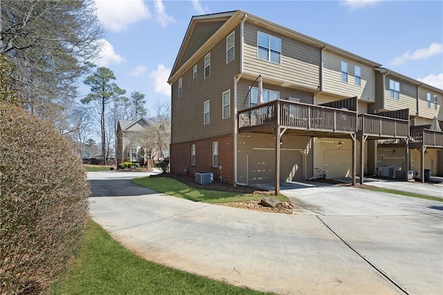 rear view of house with brick siding, central AC unit, an attached garage, and concrete driveway