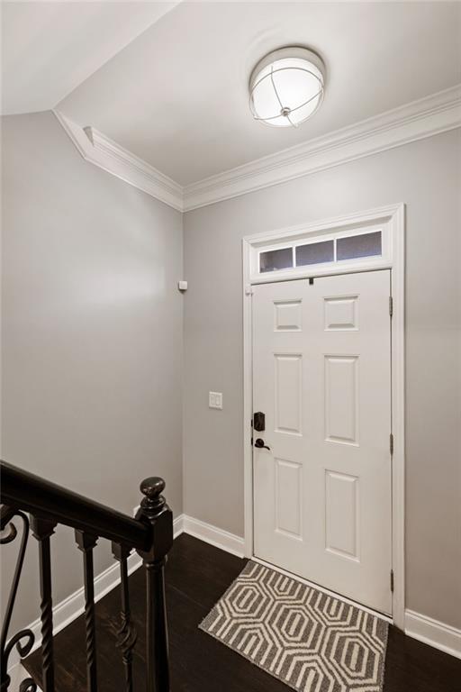 entryway with dark wood finished floors, crown molding, and baseboards