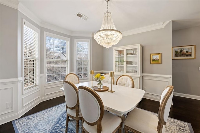 dining space with visible vents, crown molding, a chandelier, wainscoting, and dark wood-style flooring