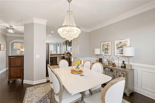 dining space with an inviting chandelier, dark wood-type flooring, crown molding, and a wainscoted wall