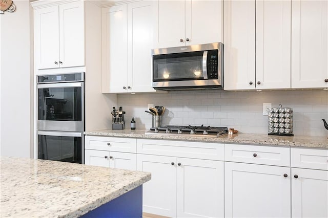 kitchen with white cabinets, decorative backsplash, light stone countertops, and appliances with stainless steel finishes