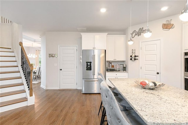 kitchen with light stone countertops, high quality fridge, a kitchen island, hardwood / wood-style flooring, and white cabinetry