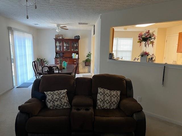 carpeted living area with ceiling fan, visible vents, baseboards, and a textured ceiling