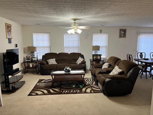 living room featuring plenty of natural light, a ceiling fan, a textured ceiling, and light colored carpet