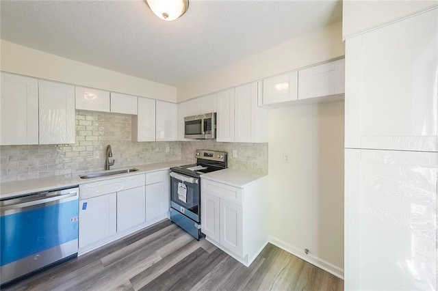 kitchen with sink, white cabinetry, light wood-type flooring, appliances with stainless steel finishes, and backsplash