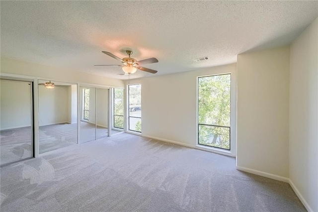 unfurnished bedroom featuring multiple windows, ceiling fan, light carpet, and a textured ceiling