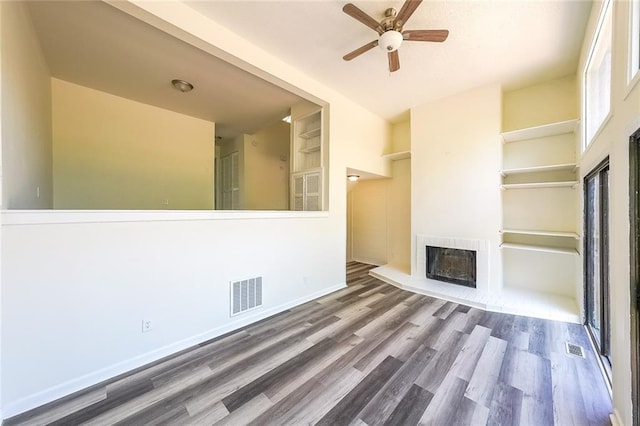 unfurnished living room with built in shelves, ceiling fan, and hardwood / wood-style floors