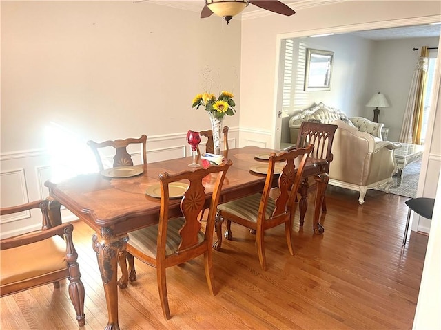 dining room featuring a ceiling fan, wainscoting, crown molding, and wood finished floors