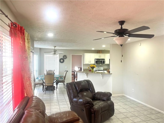 living area with ceiling fan, a textured ceiling, baseboards, and light tile patterned floors