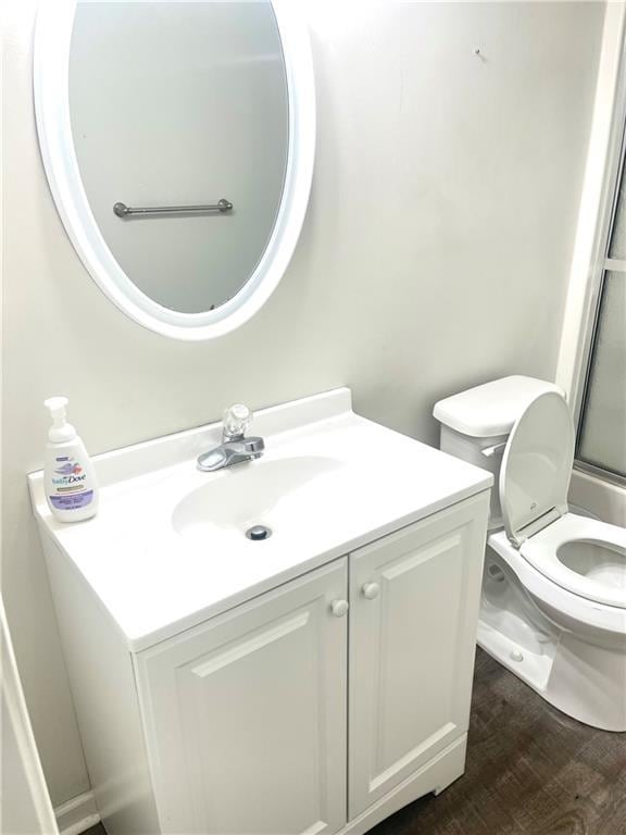 bathroom with toilet, walk in shower, wood finished floors, and vanity