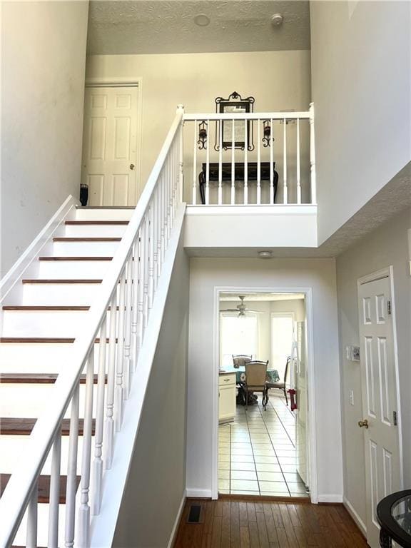 staircase featuring a towering ceiling, hardwood / wood-style flooring, baseboards, and a textured ceiling