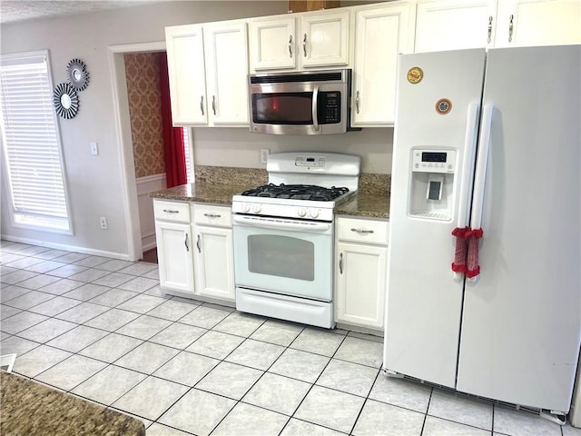 kitchen featuring white appliances, baseboards, dark stone counters, white cabinetry, and light tile patterned flooring