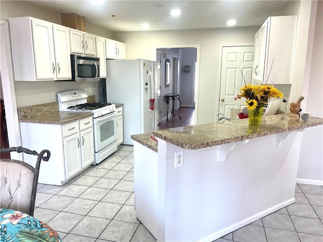 kitchen with a breakfast bar area, light tile patterned floors, white cabinets, white appliances, and a peninsula