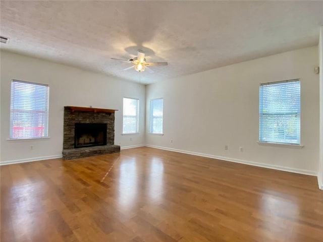 unfurnished living room with a stone fireplace, hardwood / wood-style floors, a textured ceiling, and ceiling fan