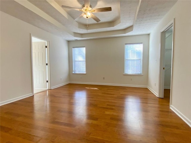 unfurnished room with a raised ceiling, hardwood / wood-style floors, and ceiling fan