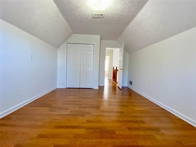 additional living space with wood-type flooring, vaulted ceiling, and a textured ceiling