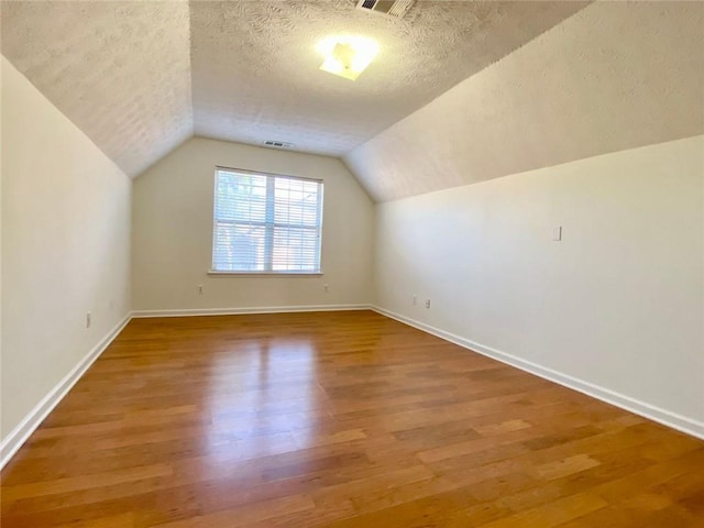 bonus room with wood-type flooring, vaulted ceiling, and a textured ceiling