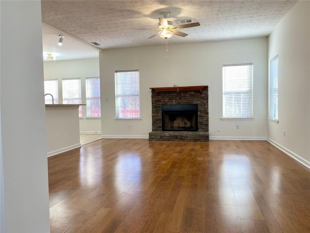 unfurnished living room with hardwood / wood-style flooring, ceiling fan, a fireplace, and a textured ceiling