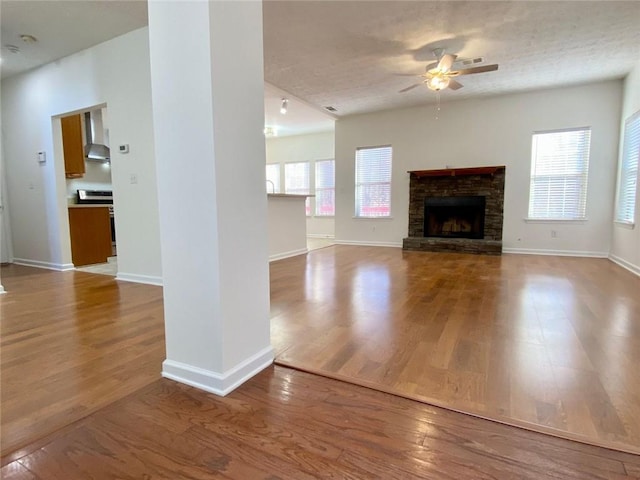 unfurnished living room with a fireplace, a textured ceiling, wood-type flooring, and ceiling fan