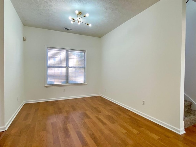 unfurnished room with a chandelier, hardwood / wood-style floors, and a textured ceiling