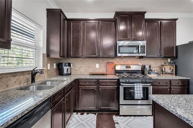 kitchen with light stone countertops, sink, dark brown cabinets, and appliances with stainless steel finishes