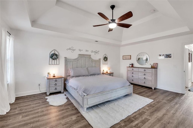 bedroom with ceiling fan, dark hardwood / wood-style floors, and a tray ceiling