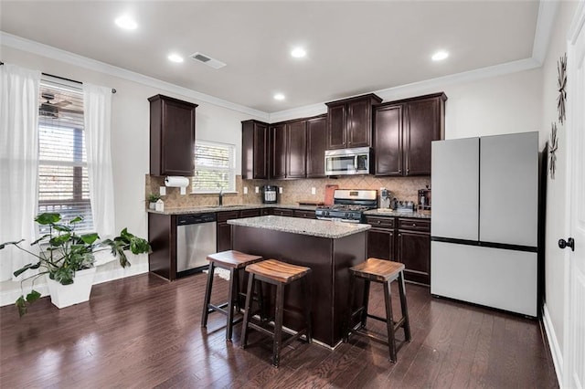 kitchen with dark hardwood / wood-style flooring, dark brown cabinets, stainless steel appliances, a kitchen island, and a breakfast bar area