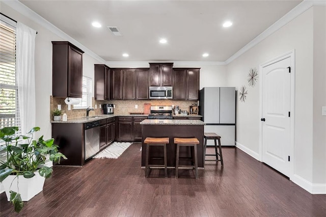 kitchen with dark brown cabinets, stainless steel appliances, a kitchen island, and ornamental molding