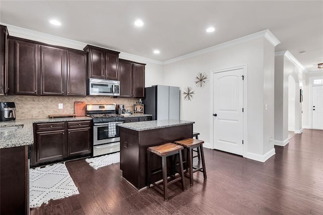 kitchen with light stone countertops, a center island, dark wood-type flooring, crown molding, and appliances with stainless steel finishes