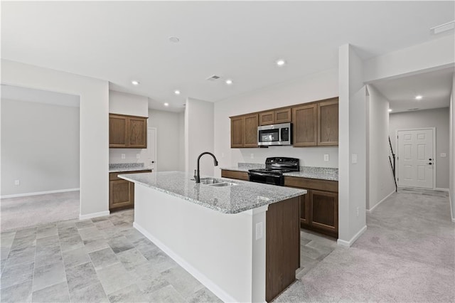 kitchen with a sink, a kitchen island with sink, stainless steel microwave, black electric range oven, and light carpet