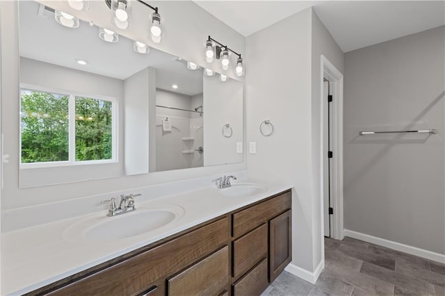 bathroom with baseboards, walk in shower, double vanity, and a sink