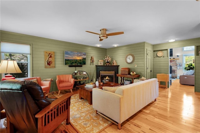 306 Pig Trl, Cherry Log, GA 30522 - living area with a warm lit fireplace, ceiling fan, wood walls, and light wood-type flooring