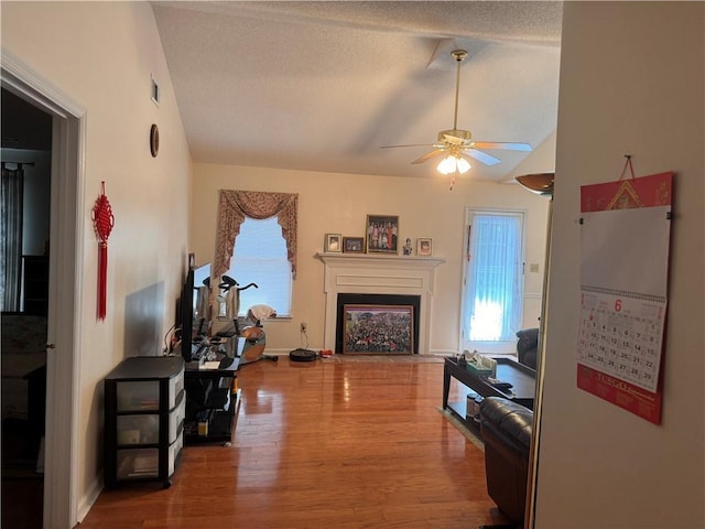 living room with ceiling fan, vaulted ceiling, a textured ceiling, and wood-type flooring