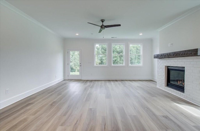 unfurnished living room featuring light wood finished floors, ornamental molding, a brick fireplace, ceiling fan, and baseboards