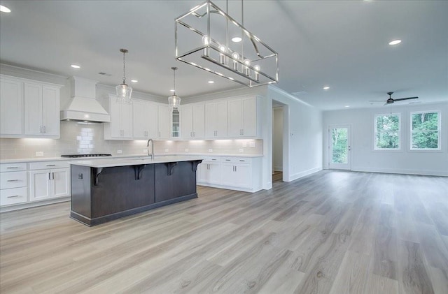 kitchen with tasteful backsplash, custom range hood, open floor plan, light countertops, and a kitchen bar