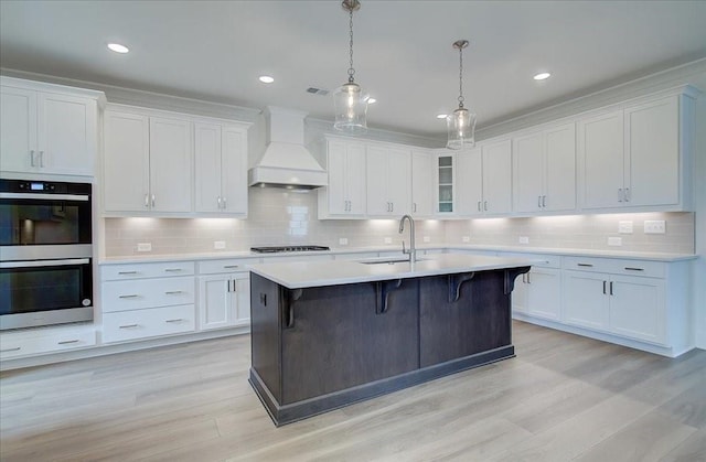 kitchen with stainless steel double oven, a sink, premium range hood, stovetop, and a kitchen bar