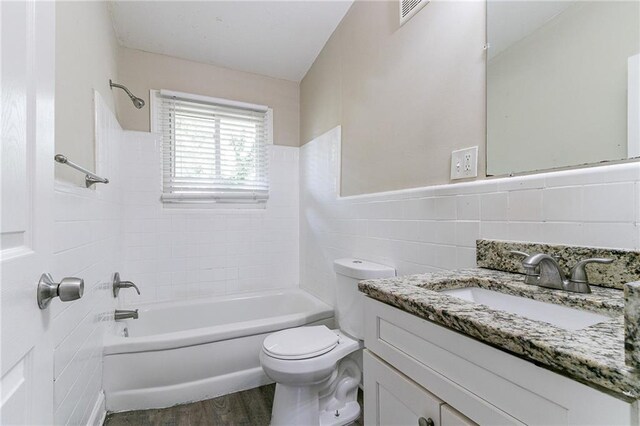 full bathroom with tile walls, vanity, wood-type flooring, toilet, and tiled shower / bath