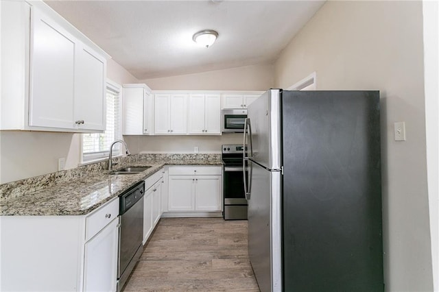 kitchen featuring light stone counters, white cabinets, sink, stainless steel appliances, and vaulted ceiling