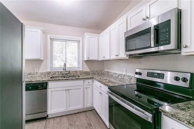 kitchen featuring light stone counters, white cabinets, sink, light hardwood / wood-style flooring, and stainless steel appliances