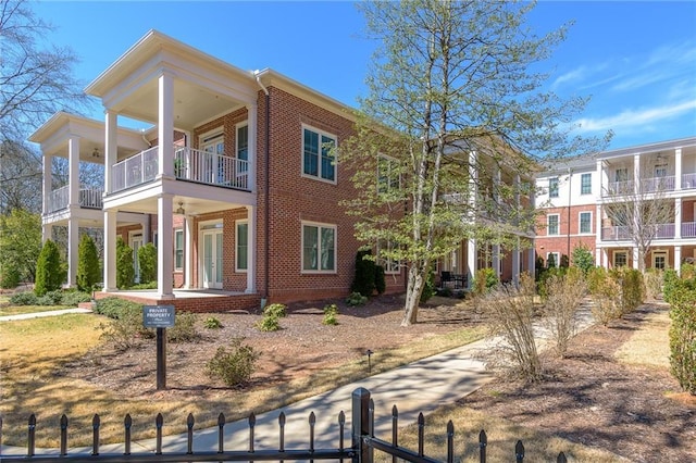 view of side of home featuring a balcony, a fenced front yard, a porch, and brick siding