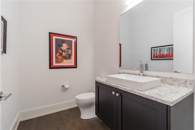 half bathroom featuring baseboards, wood finished floors, toilet, and vanity