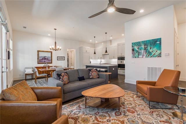 living area with dark wood finished floors, baseboards, ceiling fan with notable chandelier, visible vents, and recessed lighting