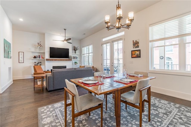 dining area featuring french doors, a fireplace, ceiling fan with notable chandelier, dark wood finished floors, and baseboards