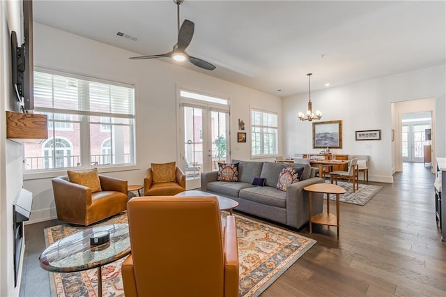 living area featuring ceiling fan with notable chandelier, visible vents, wood finished floors, and baseboards