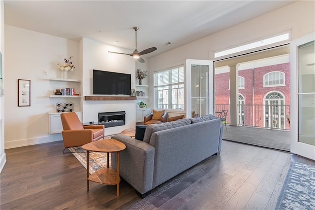 living area featuring dark wood-type flooring, baseboards, visible vents, a ceiling fan, and a glass covered fireplace