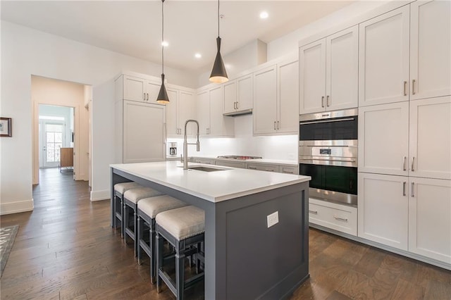 kitchen with dark wood-style floors, a sink, a kitchen island with sink, and appliances with stainless steel finishes