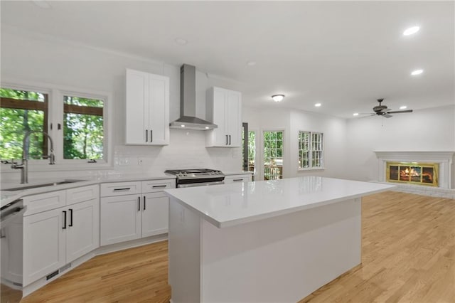 kitchen featuring a center island, white cabinets, wall chimney range hood, appliances with stainless steel finishes, and light hardwood / wood-style floors