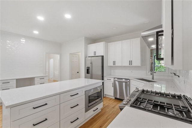 kitchen with a center island, white cabinets, sink, light wood-type flooring, and appliances with stainless steel finishes