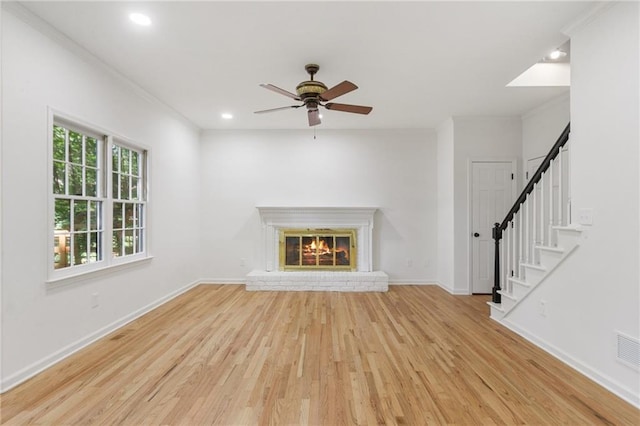 unfurnished living room featuring ceiling fan, a fireplace, ornamental molding, and light wood-type flooring